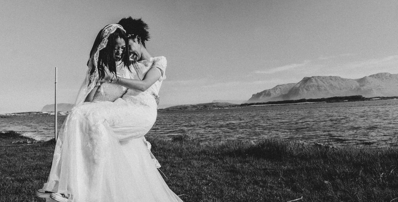 Black and white candid of two brides laughing by the lagoon