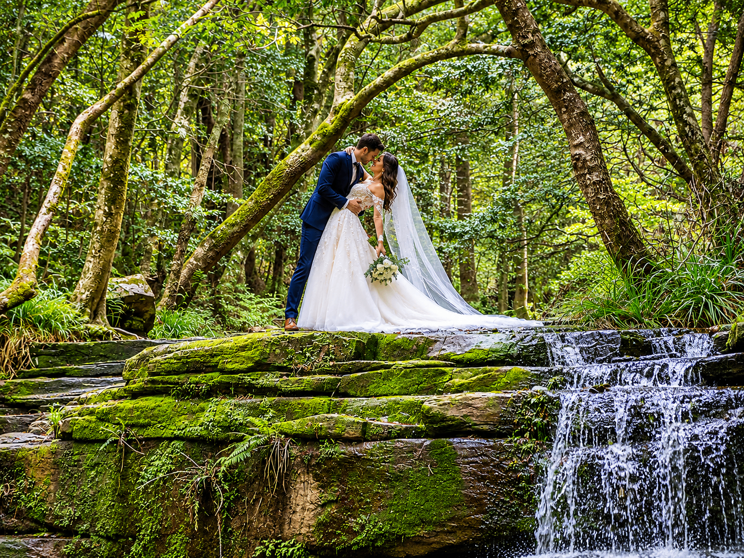 Bride and groom kissing beside a forest waterfall